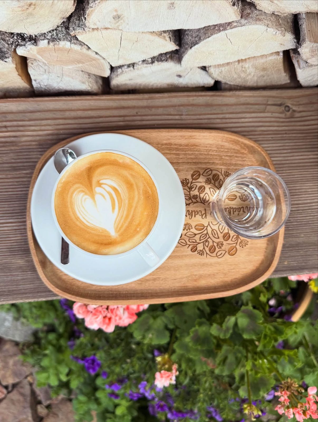 Cappuccino s latte art na dřevěném podnosu nad kvetoucí zahradou